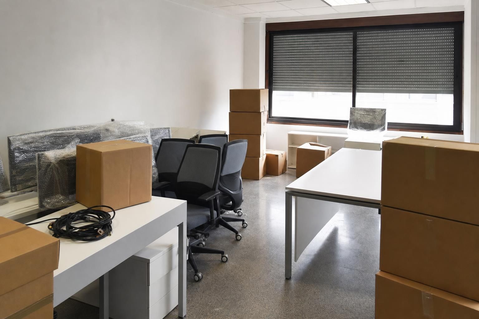 Oficina pequeña a medio embalar, con pantallas envueltas y cajas de archivo apiladas
